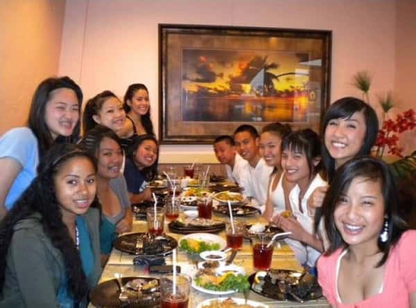 A group of friends and family gathered around a large table at a restaurant, enjoying a meal together and smiling for the photo, creating a warm and lively dining atmosphere.