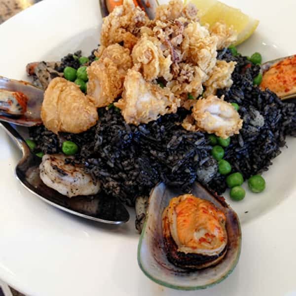 A flavorful seafood dish with mussels, shrimp, and squid served over rich black rice and vegetables.