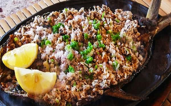 A baked fish fillet topped with seasoned garlic crumbs and fresh herbs, served with lemon wedges for a flavorful and aromatic seafood dish.