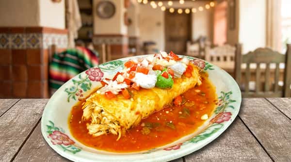 A beautifully plated enchilada dish topped with vibrant red sauce, melted cheese, fresh sour cream, and guacamole. The presentation is colorful and inviting, highlighting bold, authentic flavors.