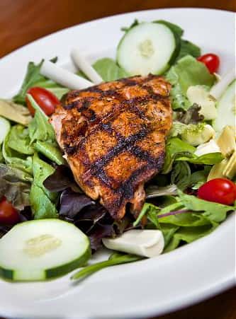 piece of blackened chicken over a salad with cucumbers and tomatoes