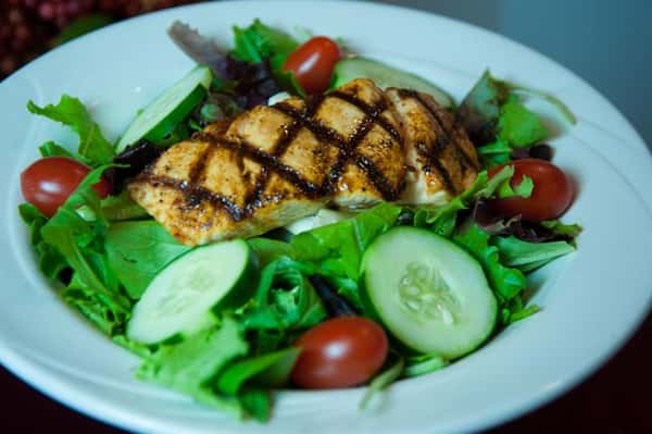 piece of blackened chicken over a salad with cucumbers and tomatoes