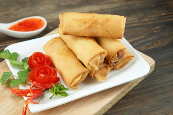 Fried spring rolls served with dipping sauce and vegetable garnish.