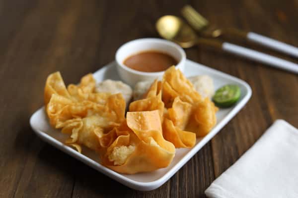 Crispy fried wontons served with dipping sauce on a white plate.