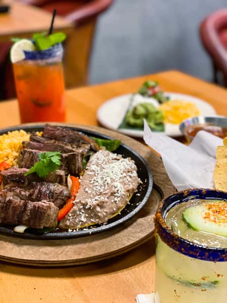 sizzling steak fajitas with grilled peppers and onions served with rice, beans, and tortillas