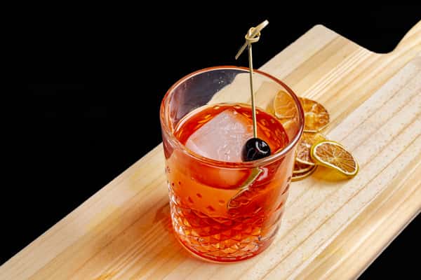 oaxaca old fashioned cocktail with orange peel and cherry in a rocks glass on a wooden board