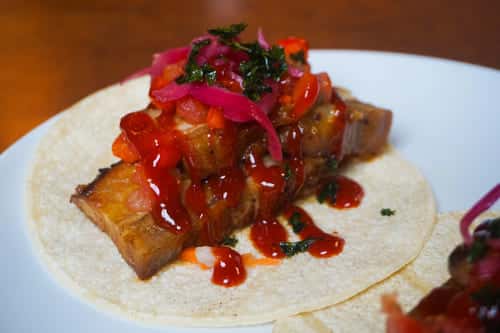 Smoky pork belly taco with tangy barbecue sauce, pickled red onions, and fresh salsa atop a corn tortilla—ideal for bold barbecue-inspired cuisine.