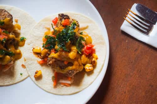 Vegetarian taco filled with grilled cauliflower, roasted corn, diced peppers, and drizzled with cheddar cheese sauce on a warm tortilla.