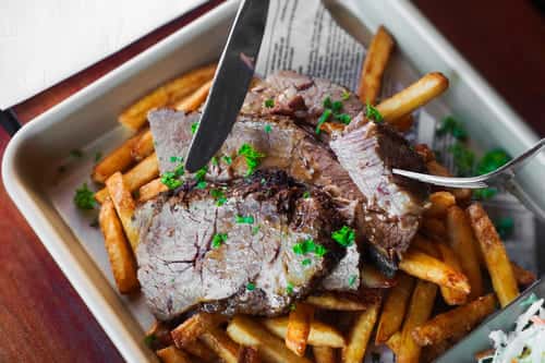 Slices of slow-cooked beef brisket layered over seasoned fries, garnished with fresh herbs for a hearty, indulgent entrée.