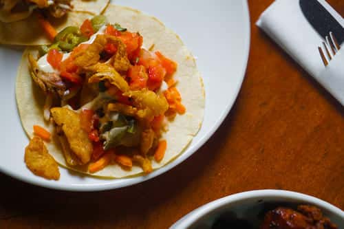 Crispy chicken taco topped with diced tomatoes, jalapeños, shredded cheese, and creamy sauce on a soft corn tortilla—perfect for Tex-Mex flavor lovers.