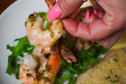 Hand holding a grilled shrimp over a bed of fresh arugula, accompanied by garlic toast—ideal for seafood and appetizer menus.