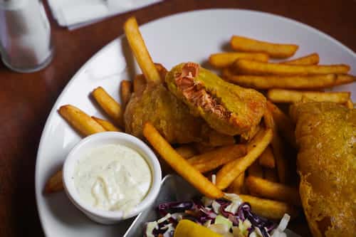 Classic fish and chips plate with crispy battered fish fillets, French fries, coleslaw, and a side of creamy tartar sauce.