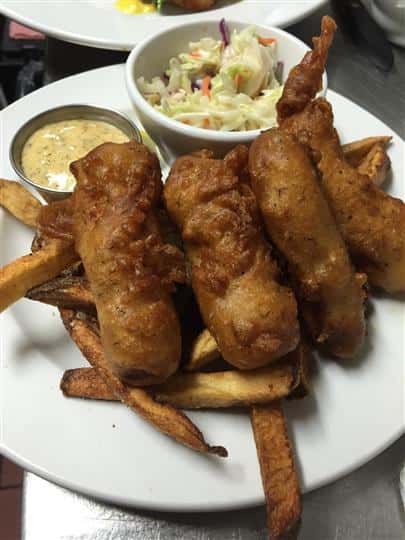 Fish and chips dish with battered and deep fied pieces of fish served with a side of tartar and coleslaw over fries