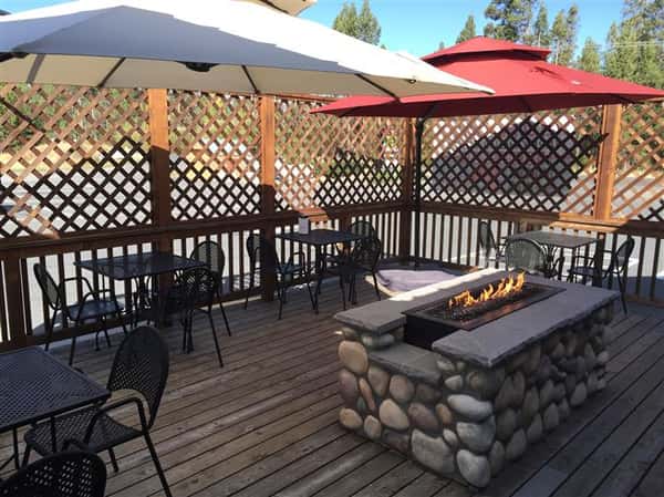 Outdoor patio with a stone wall fireplace in the middle and large umbrellas shading the tables
