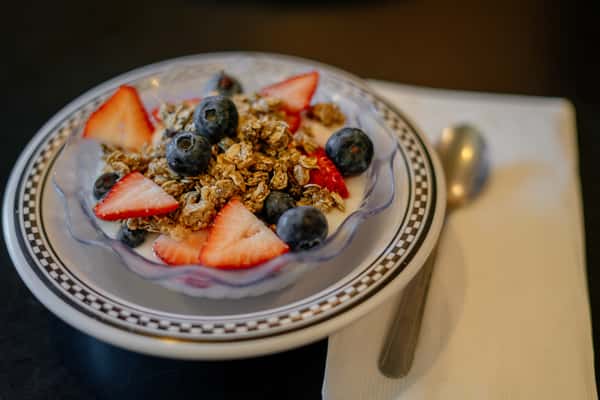 A fresh and colorful yogurt parfait bowl topped with sliced strawberries, blueberries, crunchy granola, and shredded coconut. This light and wholesome dish offers a refreshing option for a healthy breakfast or midday snack.
