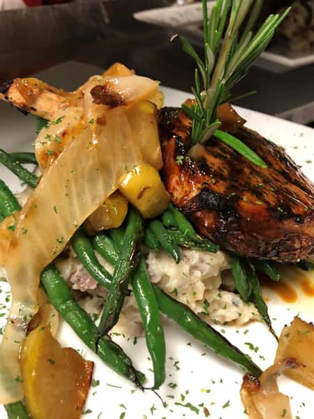 a barbecue chicken slice next to mashed potatoes, string beans, and onions on a plate