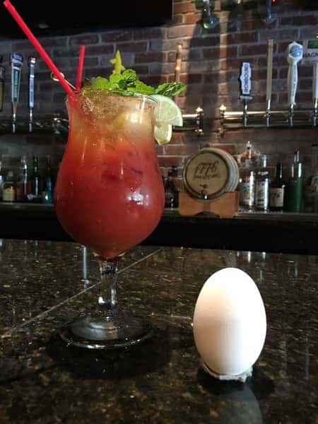 a bloody mary in a glass with two slices of lemon and garnish next to an egg