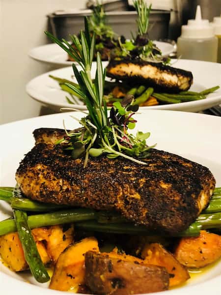 grilled fish on a bed of sweet potatoes and asparagus on a white plate