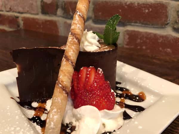 a chocolate frozen dessert next to a sliced strawberry and whipped cream and chocolate syrup
