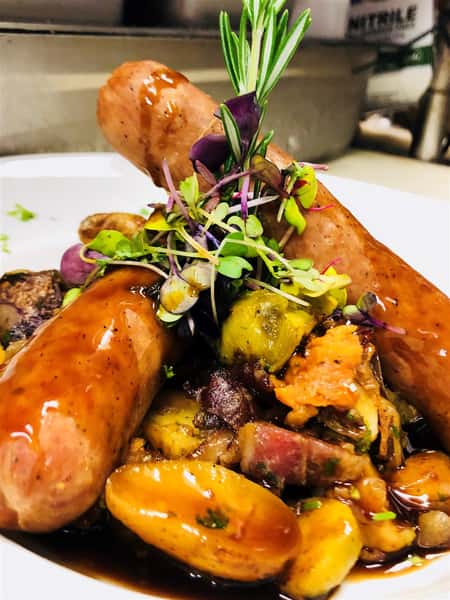 two sausage links on a plate with potatoes and gravy on a white plate and garnished