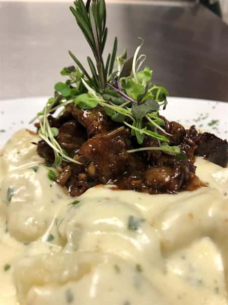 noodles in a creamy sauce with a pile of meat in brown gravy garnished on a white plate