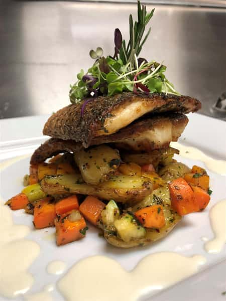 fish stacked on top of vegeteables on a plate and garnished