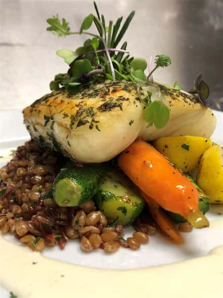 a grilled fish on a bed of a zucchini, carrot, lemon, and rice on a white plate with cream sauce and garnished