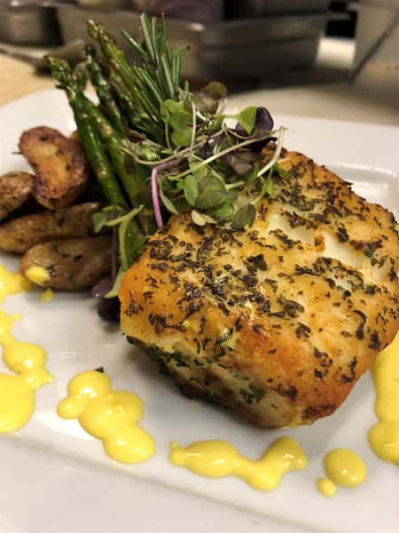 a grilled fish on top of a bed of vegetables in a cream sauce and garnished on a white plate