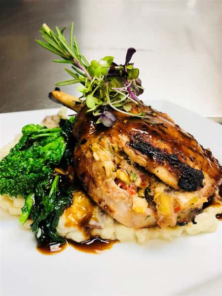 ribs stuffed with vegetables on a pile of mashed potato and gravy with broccoli and spinach on a white plate and garnished