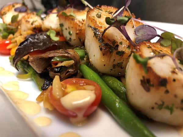 four scallops lined on a plate with vegetables