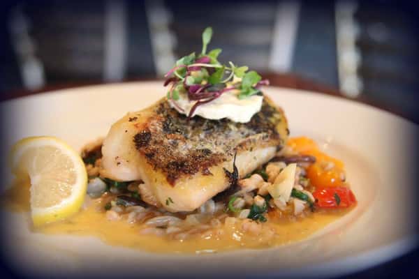 Pan seared cod over white beans and roasted peppers with a lemon wedge