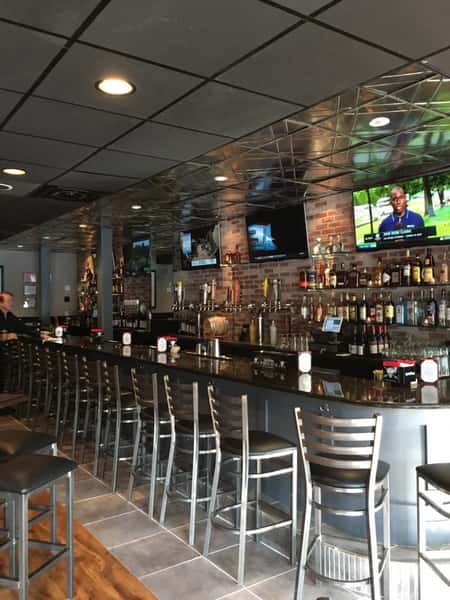 Interior bar area with chairs set up at the bar, TV's hanging on the wall and an assortment of liquor bottles behind the bar