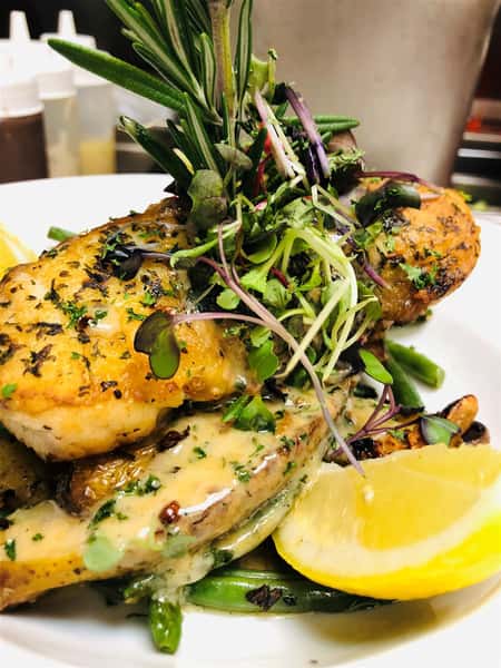 a slice of fish on creamy sauce on a bed on potatoes and asparagus with a lemon wedge