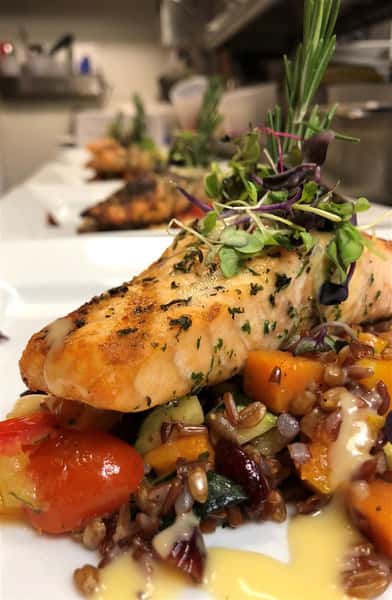 a grilled fish on top of a bed of vegetables in a cream sauce and garnished on a white plate