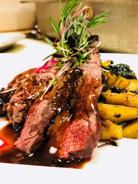 rare steak on a plate with steak sauce, a side of potatoes on a white plate and garnished