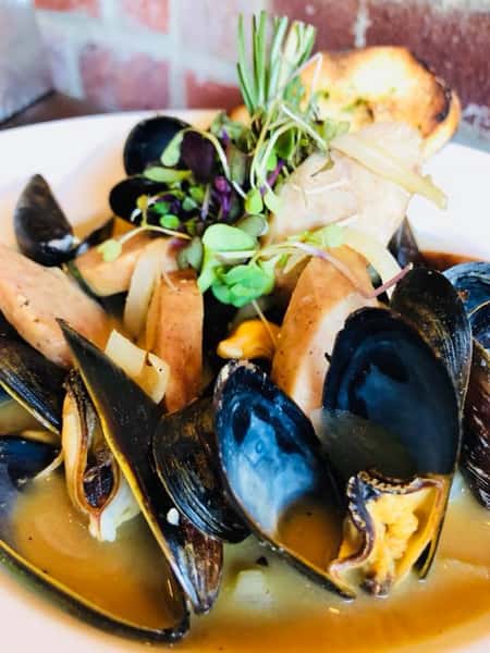 Steamed mussles in a bowl with toasted bread slices and assorted greens