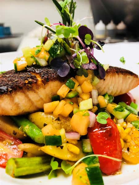 grilled fish on a bed of mixed vegetables and garnished on a white plate