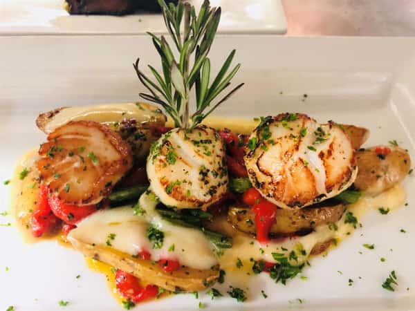 three scallops covered in white sauce with potatoes, asparagus and peppers on a plate and garnished
