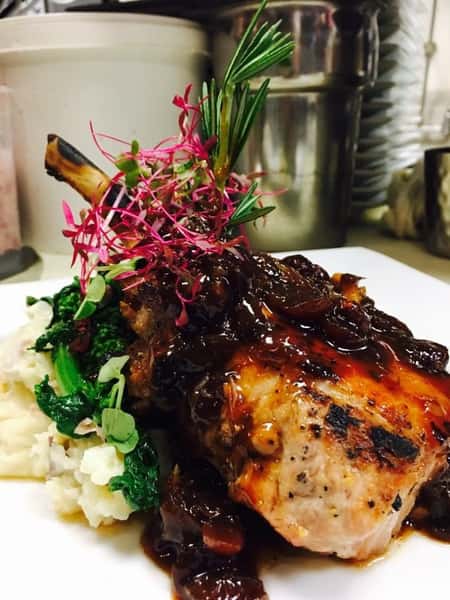 spare rib on a plate with mashed potatoes and spinach covered in gravy and garnished on a white plate