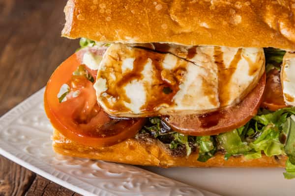 Caprese-style sandwich with fresh mozzarella, tomato, mixed greens, and balsamic glaze on toasted artisan bread.