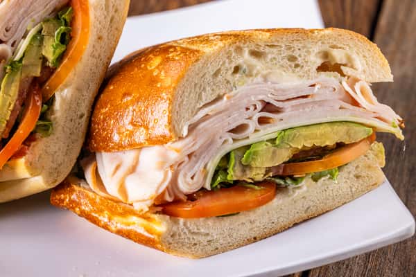 Turkey and avocado deli sandwich on toasted artisan bread with fresh tomato, lettuce, and sliced turkey breast.