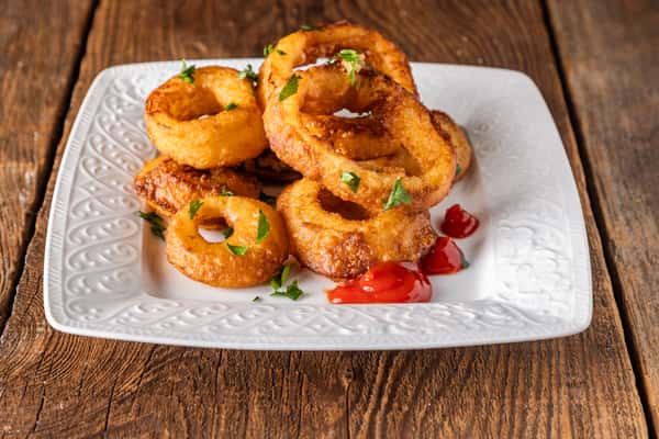 Golden crispy onion rings garnished with parsley and served with ketchup on a white plate.