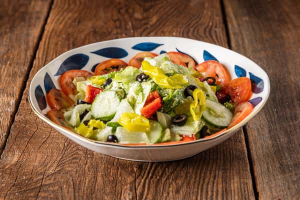 Fresh Italian garden salad with romaine lettuce, cucumbers, tomatoes, black olives, banana peppers, and grated Parmesan in a patterned bowl.