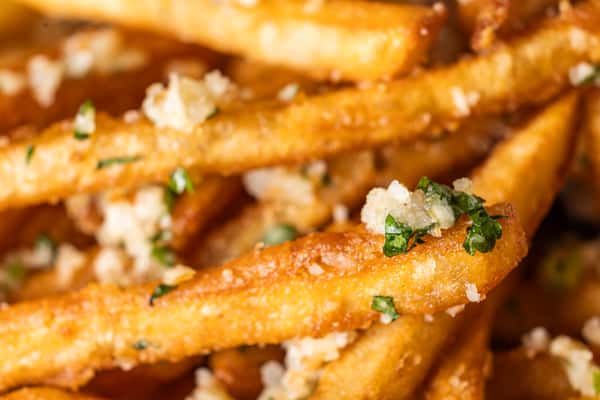 Close-up of crispy garlic Parmesan French fries topped with chopped parsley.