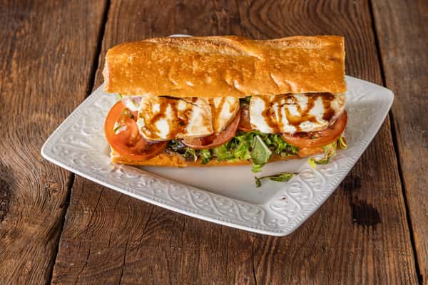 Caprese sandwich with fresh mozzarella, tomatoes, mixed greens, and balsamic glaze on toasted artisan bread served on a white plate.