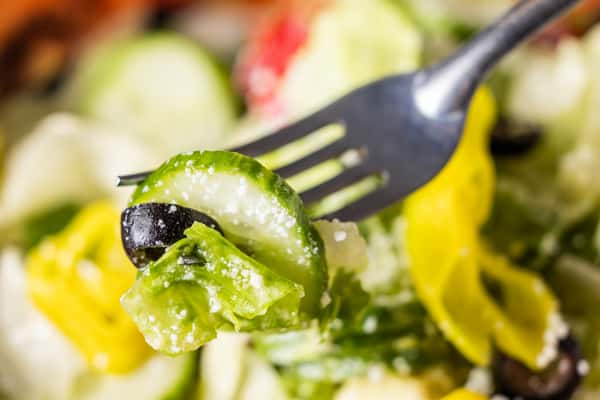 Close-up of a fork lifting fresh Italian chopped salad with cucumber, olives, banana peppers, lettuce, and grated Parmesan.