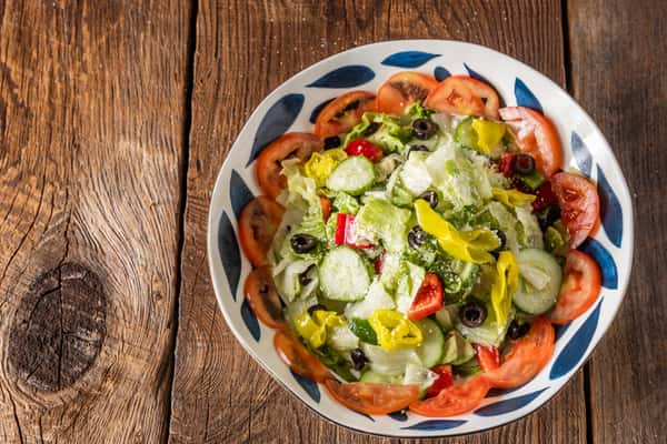 Italian chopped salad with romaine lettuce, cucumbers, tomatoes, black olives, banana peppers, and grated Parmesan in a patterned bowl.