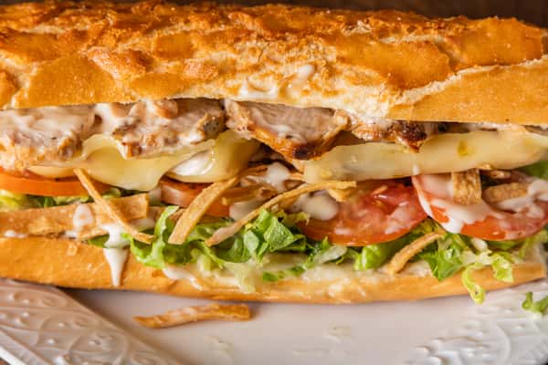 Close-up of grilled chicken sandwich with melted cheese, lettuce, tomato, and crispy potato sticks on toasted bread.