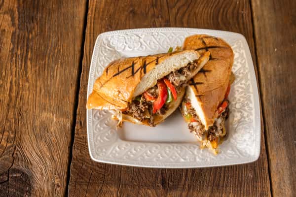 Grilled Philly cheesesteak sandwich with shaved steak, sautéed onions, melted cheese, and bell peppers on toasted bread.