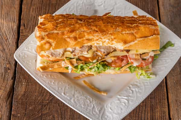 Grilled chicken sub sandwich with melted cheese, lettuce, tomato, crispy potato sticks, and creamy garlic sauce on toasted bread.